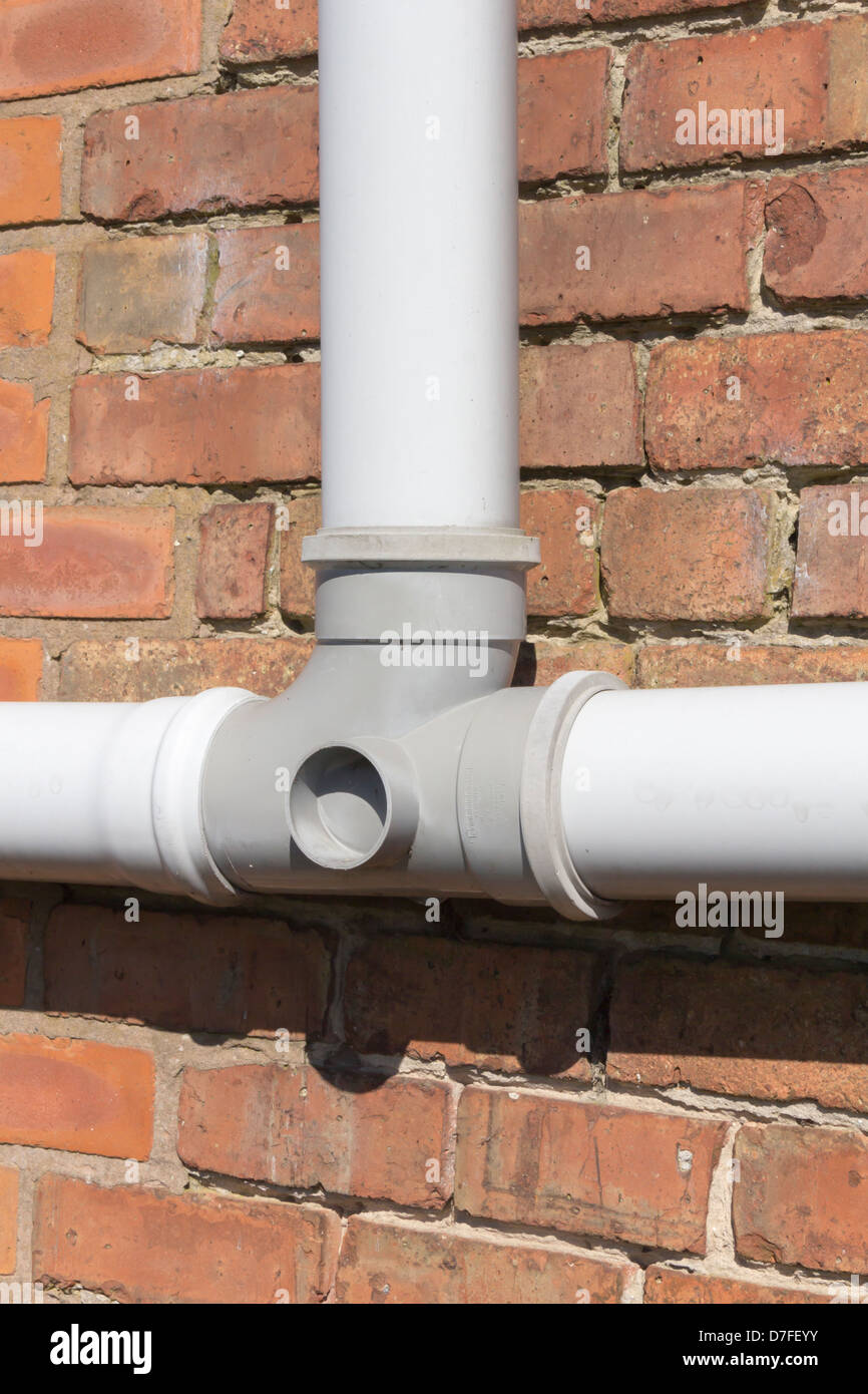Grey plastic (Polyvinyl Chloride, un-plasticised - PVC-U) drainpipe T piece section, mounted horizontally on a brick wall. Stock Photo