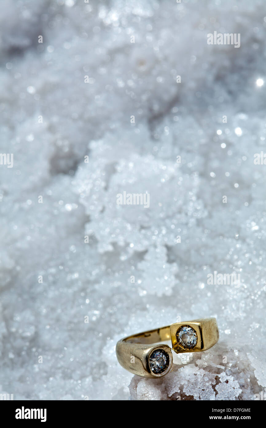 A gold/white gold ring inlaid diamonds resting on salt flakes bedding. Shot on beach infamously salty Dead Sea in Israel. Stock Photo