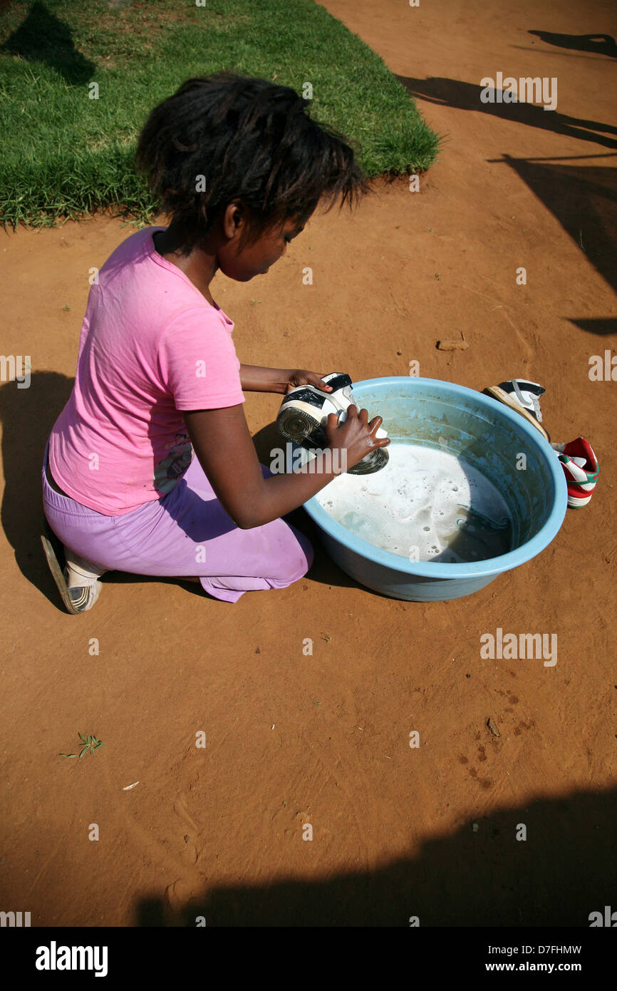 An African girl scrubs her shoes clean in a dish of soapy water Stock