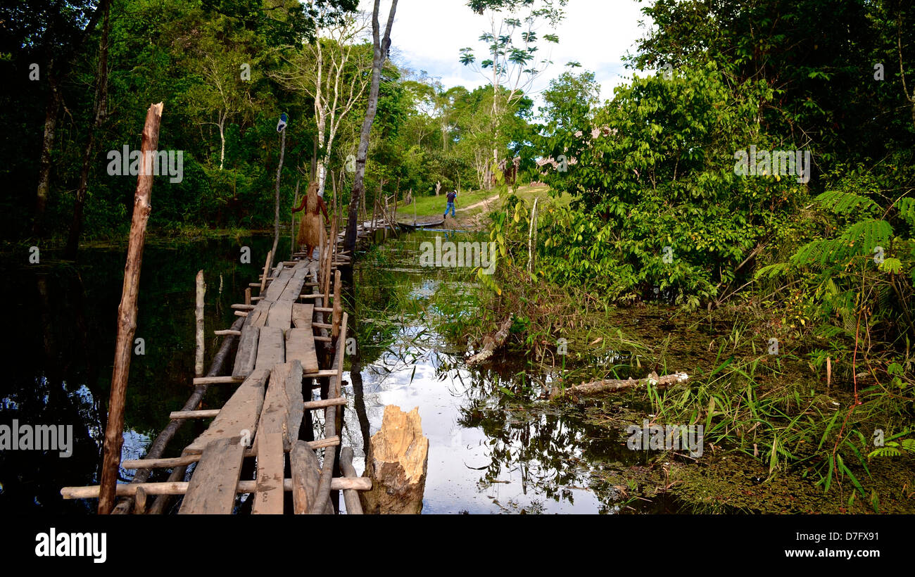 a member of the Yagua indigenous tribe crosses a bridge in the Amazon rain forest, Peru Stock Photo