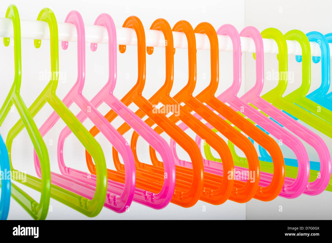 Colored plastic hangers hanging on a rod in an empty white closet Stock