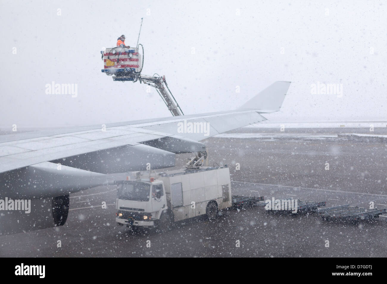 Technical staff in airport de-icing aircraft wings with fluid during strong blizzard. Stock Photo