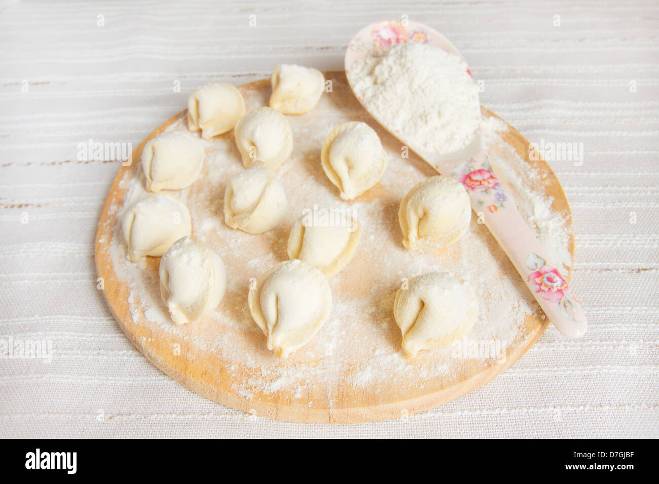 Uncooked dumplings (russian traditional food - pelmeni) on wooden cuting board with flour over linen background. Stock Photo