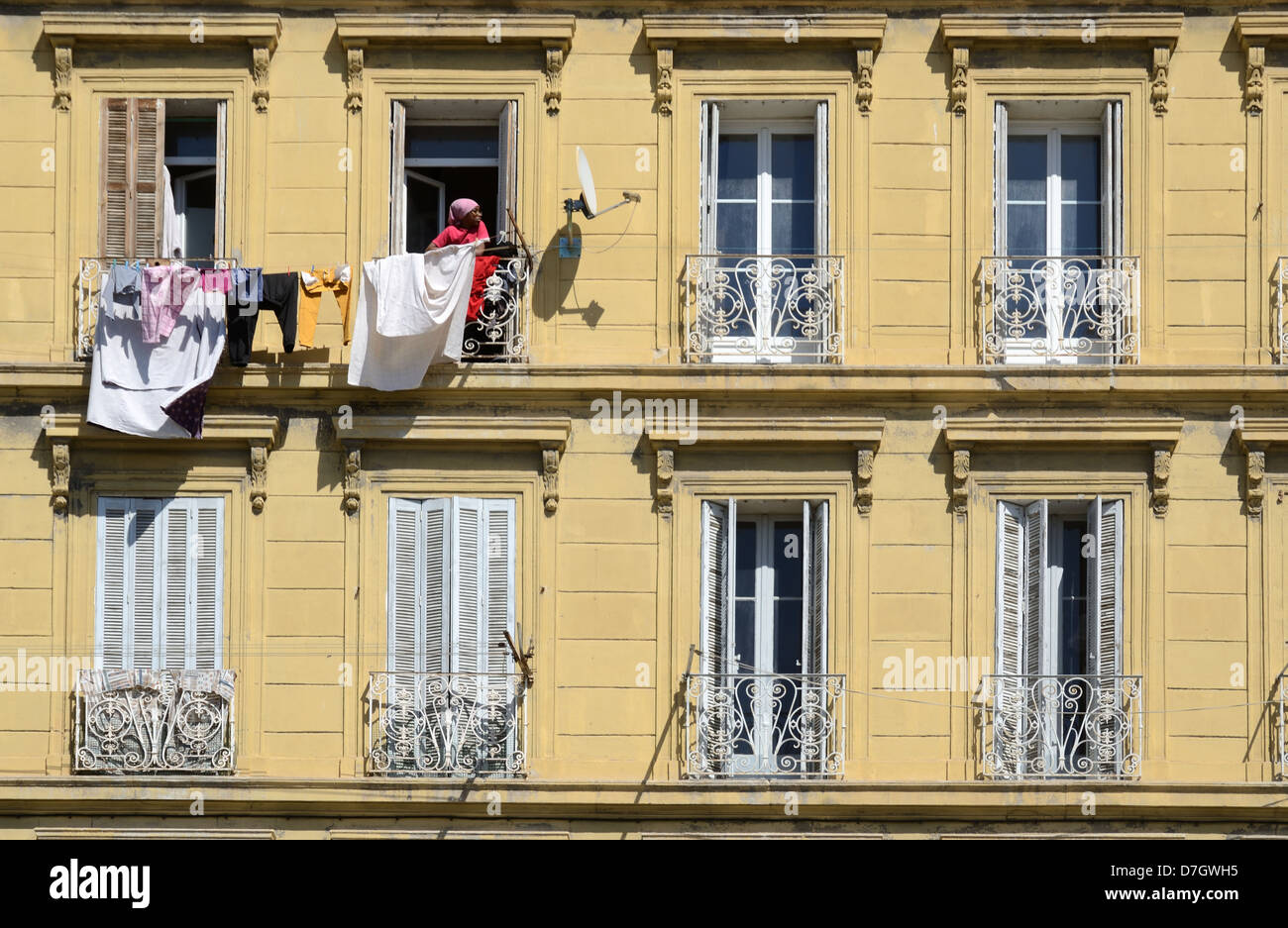 Immigrant Woman Hanging Out Washing, Clothes or Laundry to Dry Outside Traditional Apartment Building Marseille or Marseilles Provence France Stock Photo