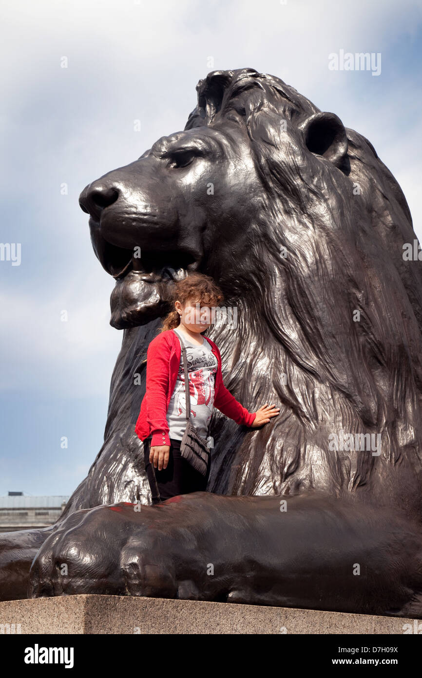 A child having her photo taken climbing on a lion statue, Trafalgar Square, Central London UK Stock Photo