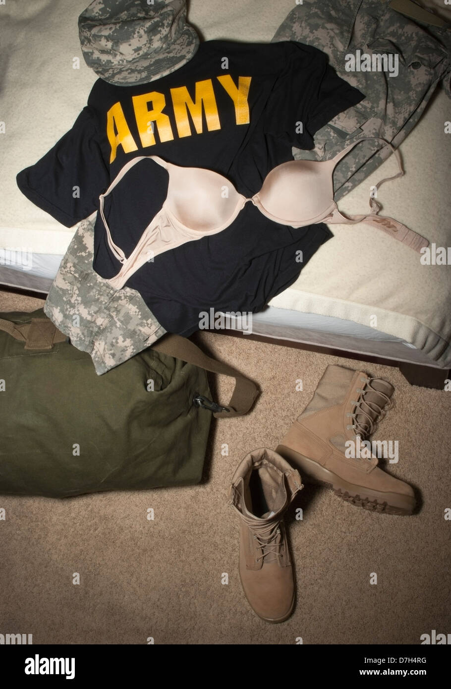 Women’s Army Combat (ACU) camouflage hat, pants, desert Combat boots, Duffel bag, tee-shirt and bra on a civilian bed. Stock Photo