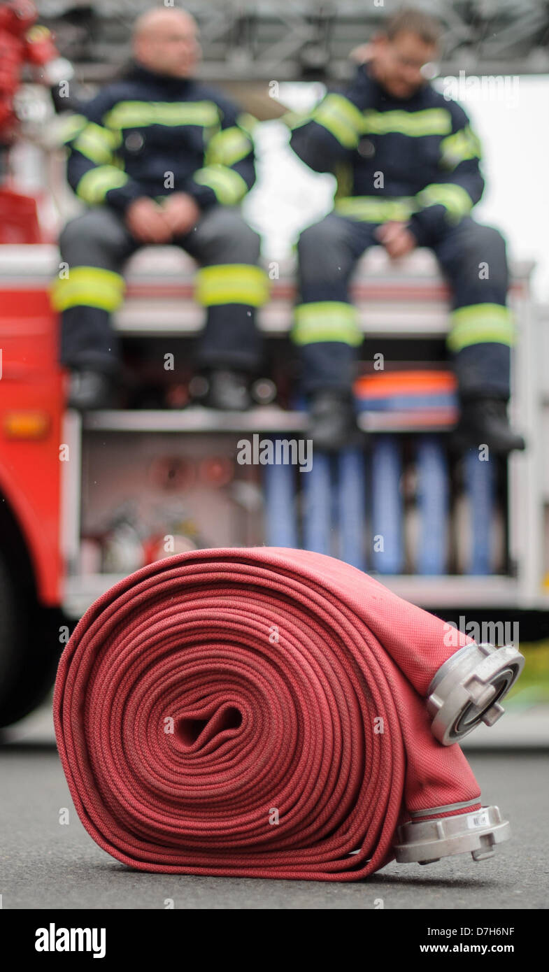 Two firemen sitting on a fire truck. In the foreground is a hose. Photo
