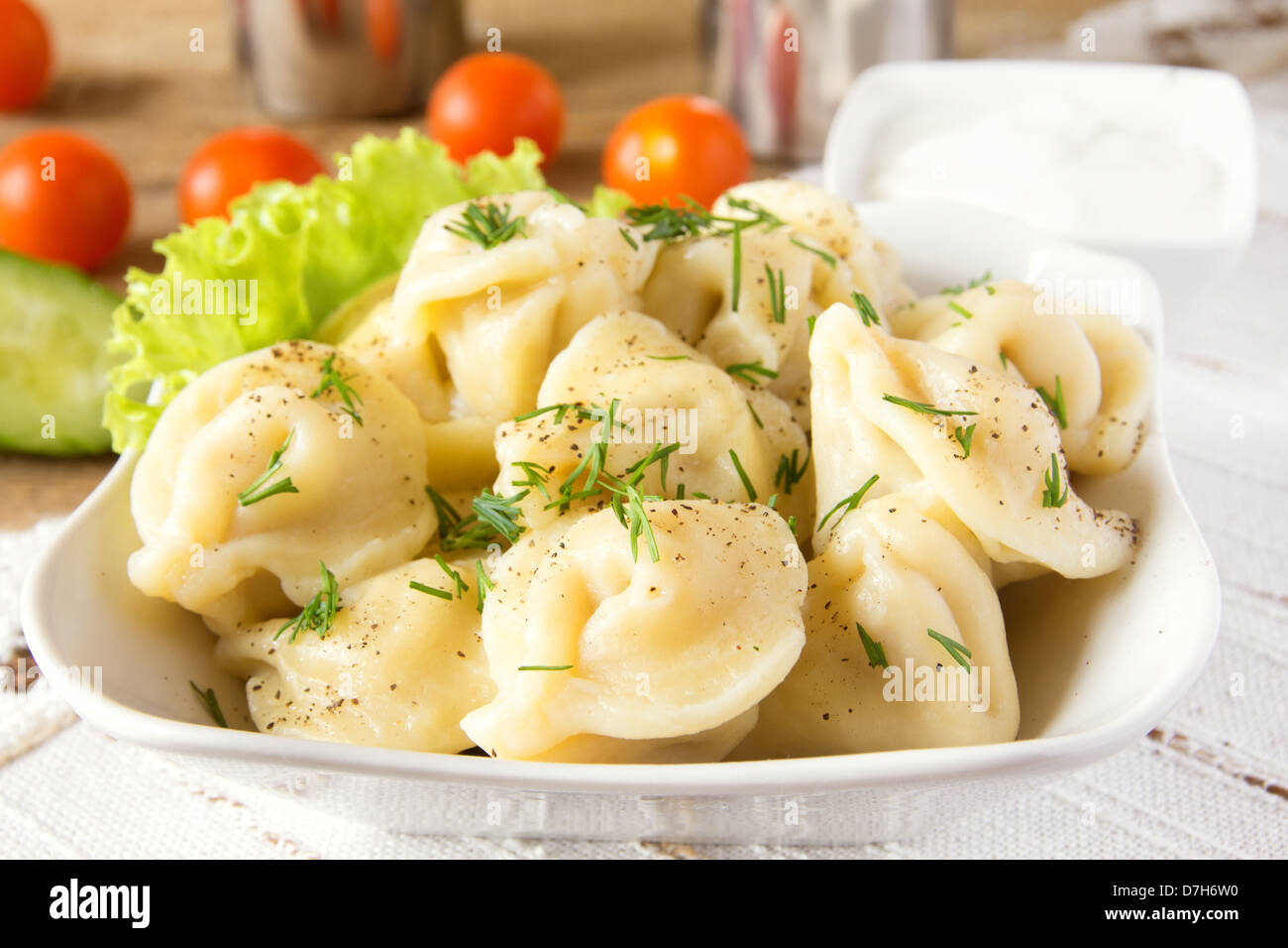 Meat dumplings (russian pelmeni) with pepper, dill (fennel), vegetables and sour cream in bowl close up. Stock Photo