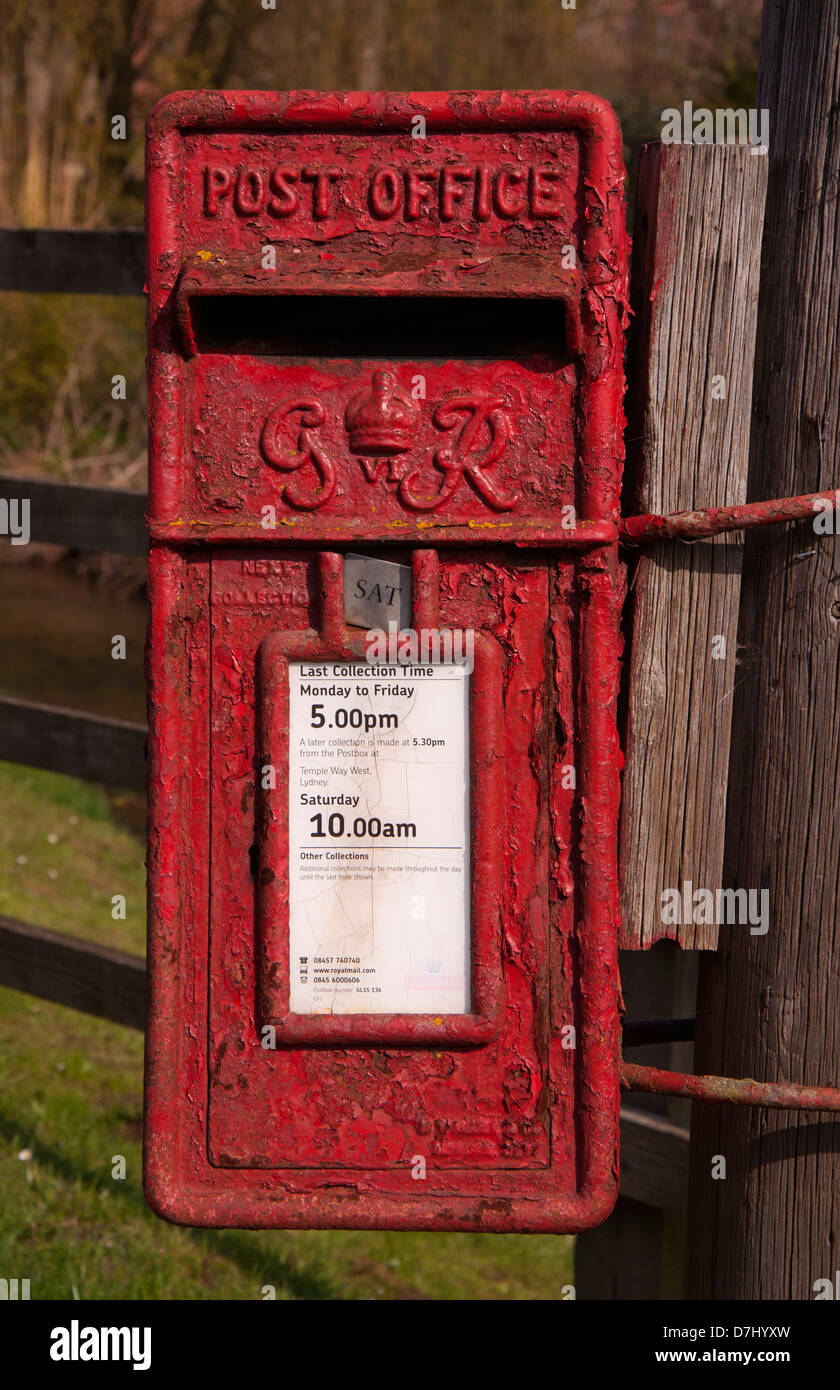 Post box. Letter box, old, dated, red, peeling paintwork, neglected, in use, fixed to concrete post, sunlit, selective focus Stock Photo
