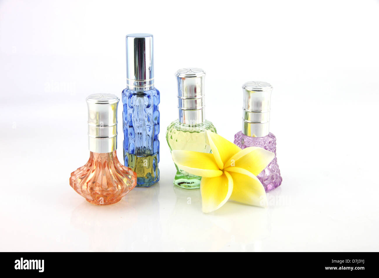 The yellow flowers and Orange,Blue,Green,Violet Perfume bottles on the white background. Stock Photo