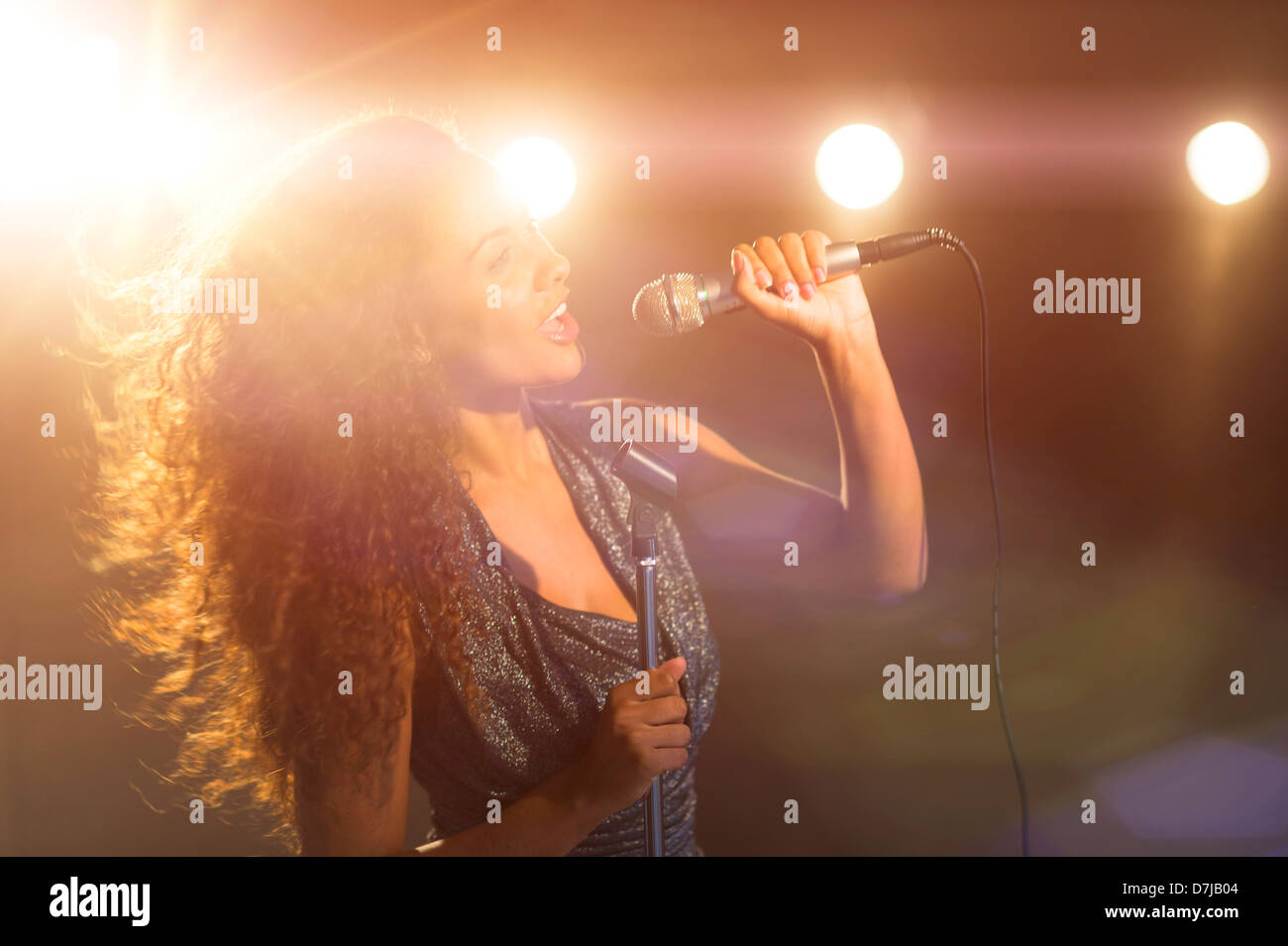 Young woman singing in spotlight Stock Photo