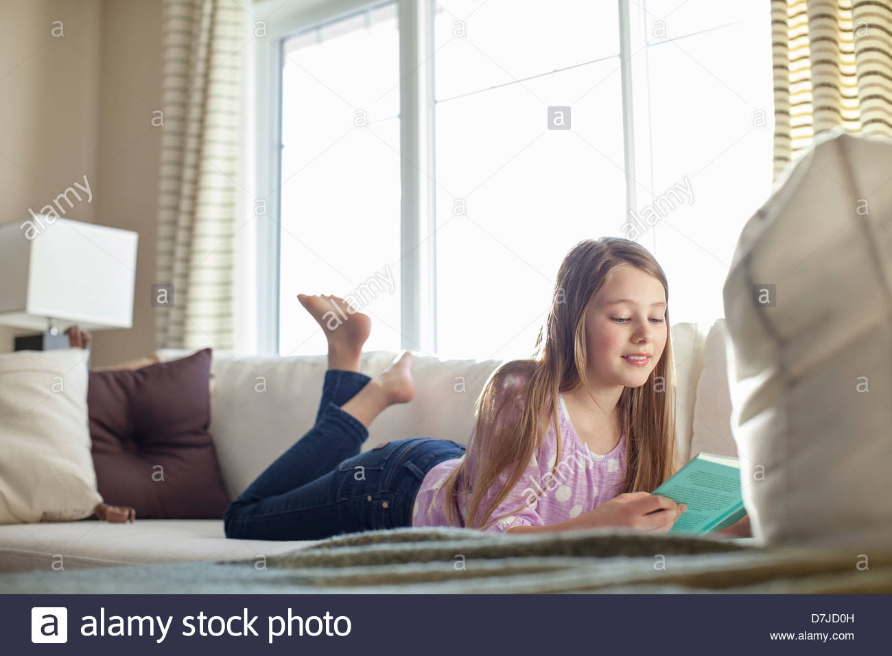 Young girl reading book lying on sofa Stock Photo