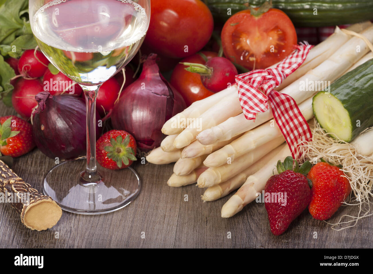 Fresh vegetables and seasonal ingredients with asparagus, onions, tomatoes a glass of white wine on a wooden background Stock Photo