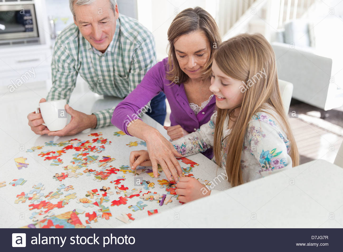 Granddaughter doing jigsaw puzzle with grandparents in kitchen Stock Photo
