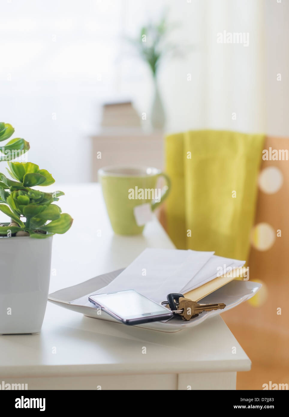 View of mug, flower pot, mobile phone, key and paper on table Stock Photo