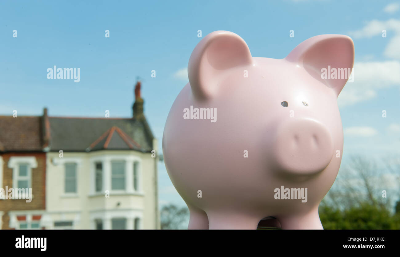 Pink piggy bank with houses behind against a blue sky. Stock Photo