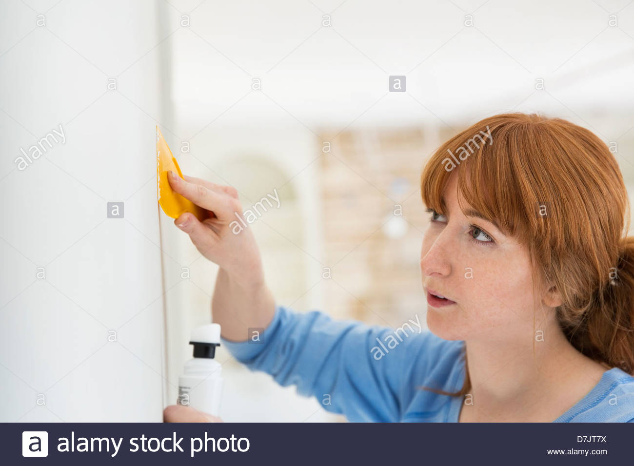 Woman applying filler to wall with putty knife in home Stock Photo