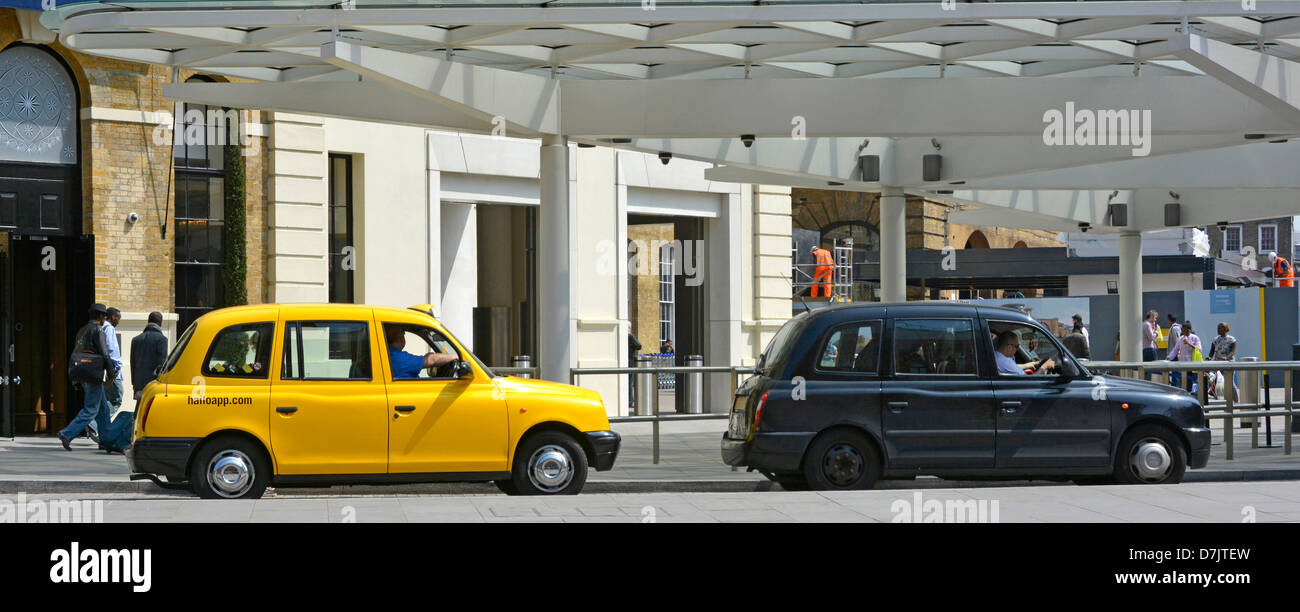 Black cab with no advertising next to a yellow taxi with advert at a London station pickup rank Stock Photo