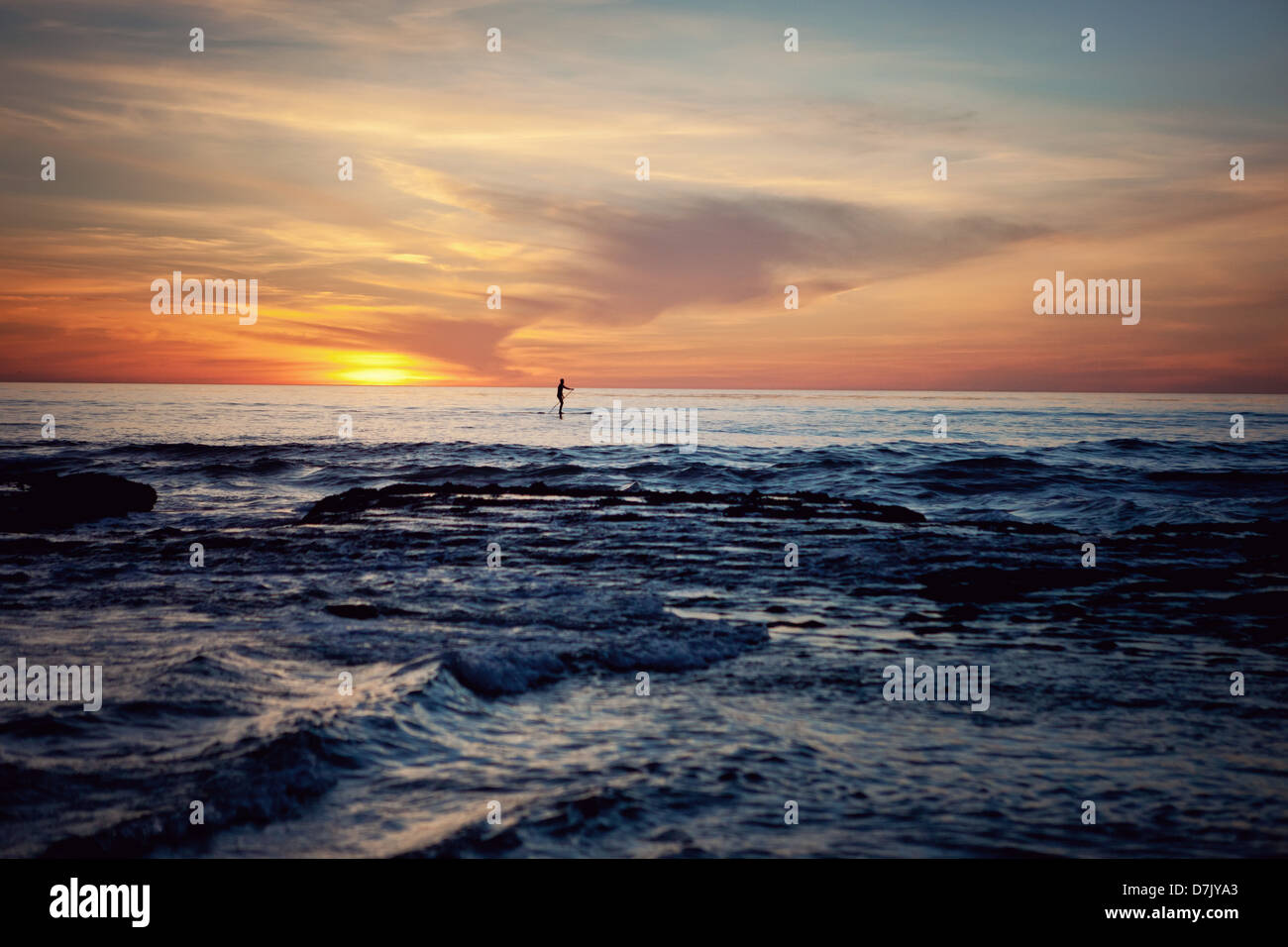 Paddle boarder in the ocean, far away in the distance at sunset Stock Photo