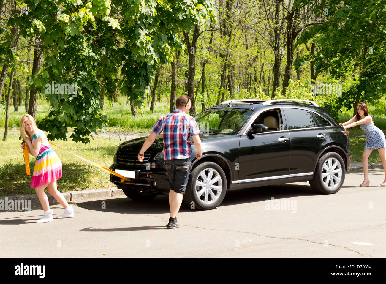 Image of beautiful females pulling and pushing a broken down car in the middle of their journey. Stock Photo