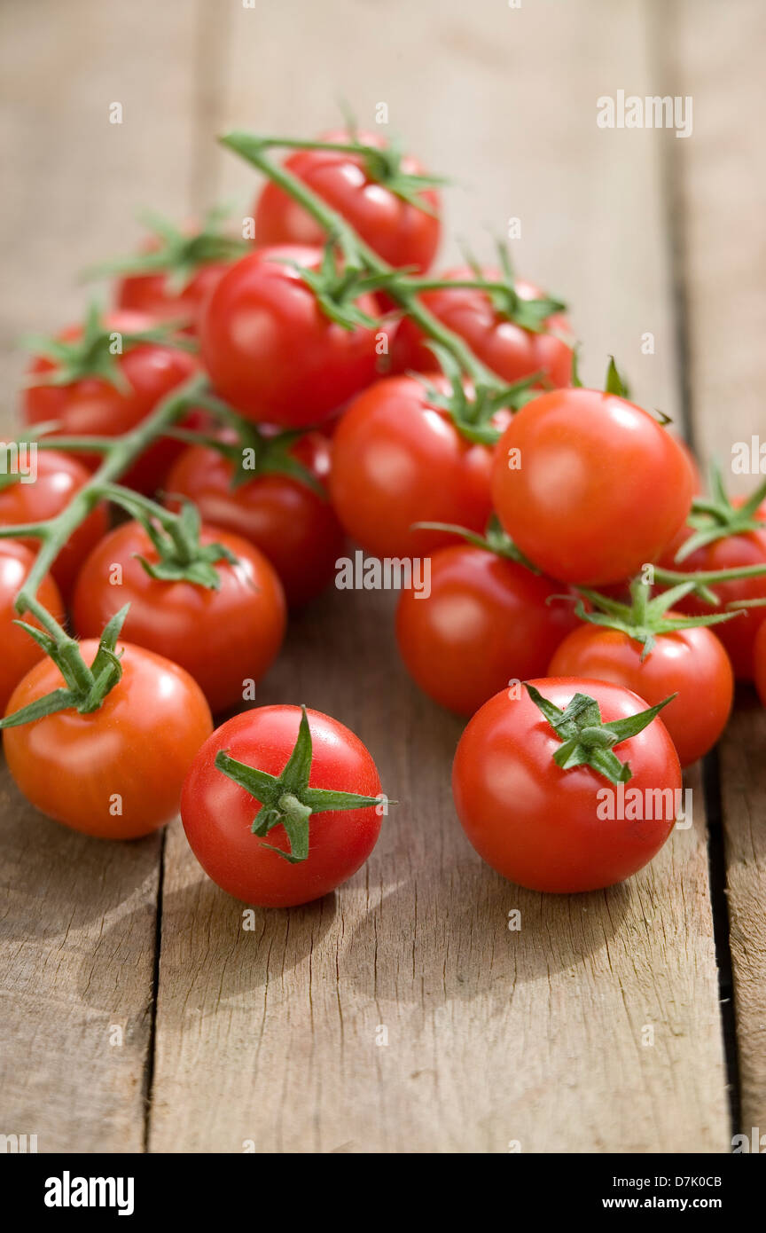 Close up of a string of vine-ripe cherry tomatoes on a rustic wooden tabletop. Stock Photo