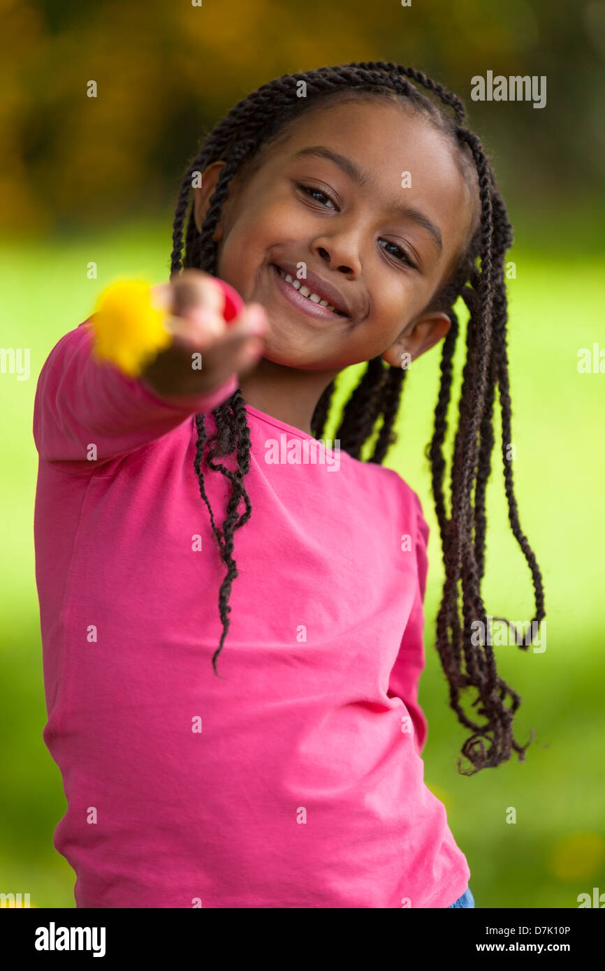 Outdoor portrait of a cute young black girl holding a dandelion flower - African people Stock Photo