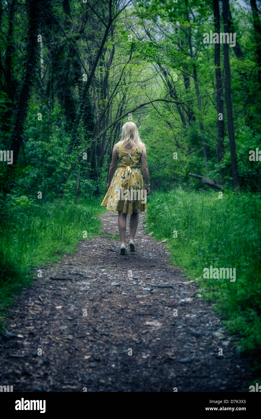a girl in a yellow dress is walking in the woods Stock Photo