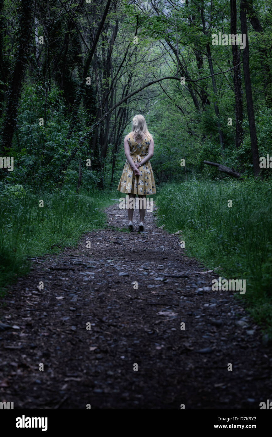 a girl in a yellow dress is standing in the woods Stock Photo