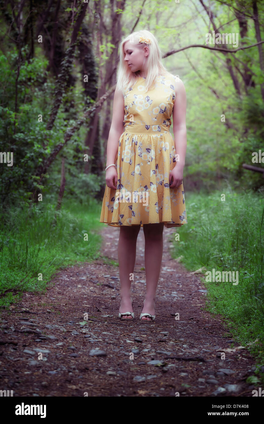 a girl in a yellow dress is standing in the woods Stock Photo