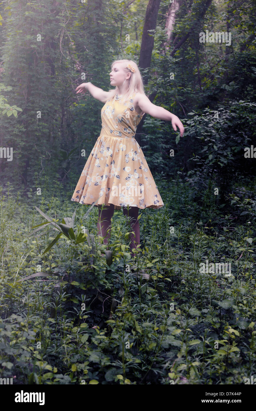 a blond girl with a yellow dress is dancing in the woods Stock Photo