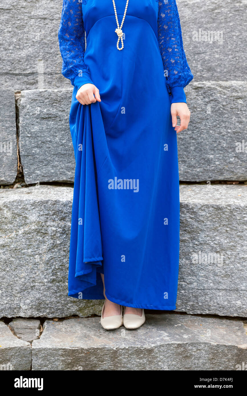 a woman in a blue dress is standing on stone steps Stock Photo