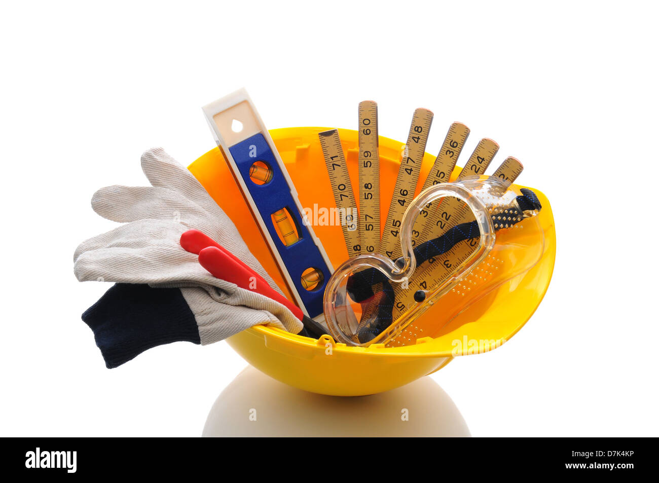 A yellow contractors hard hat with work gloves and tools inside. Horizontal format over white with reflection. Stock Photo