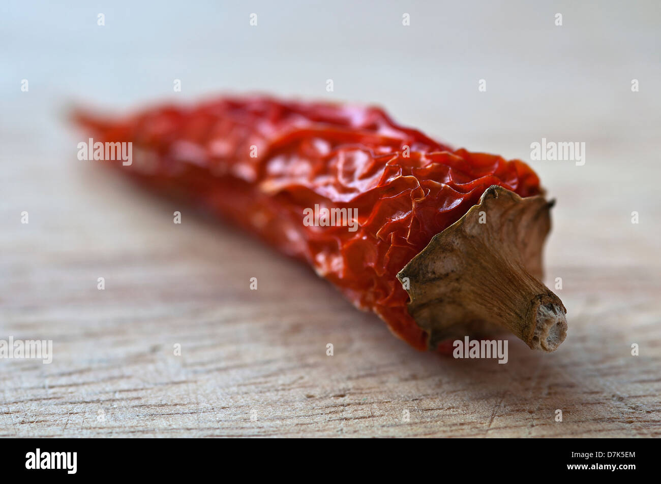 Naturally lit macro image of a dried whole chilli, lay on a wooden chopping board Stock Photo