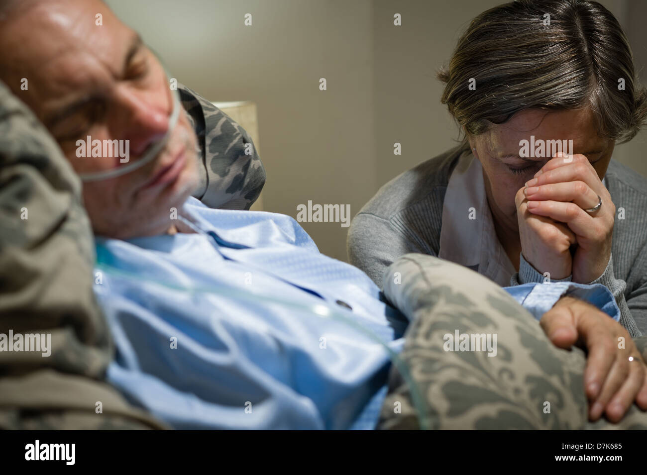 Old wife praying for terminally ill husband lying in coma Stock Photo