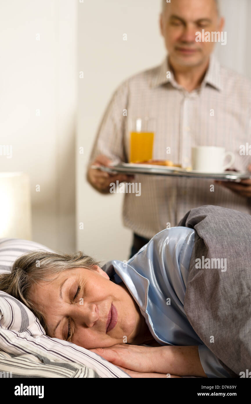 Loving senior husband serving breakfast to sleeping wife Stock Photo