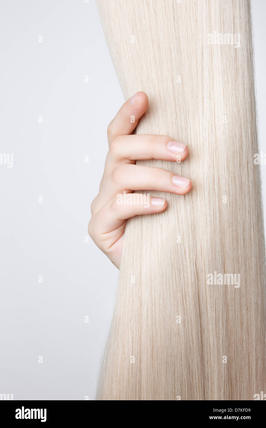 Human hand holding blond hair against white background, close up Stock Photo