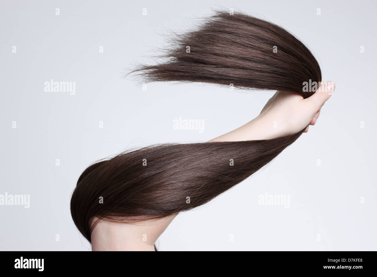 Human hand holding brown hair against white background, close up Stock Photo