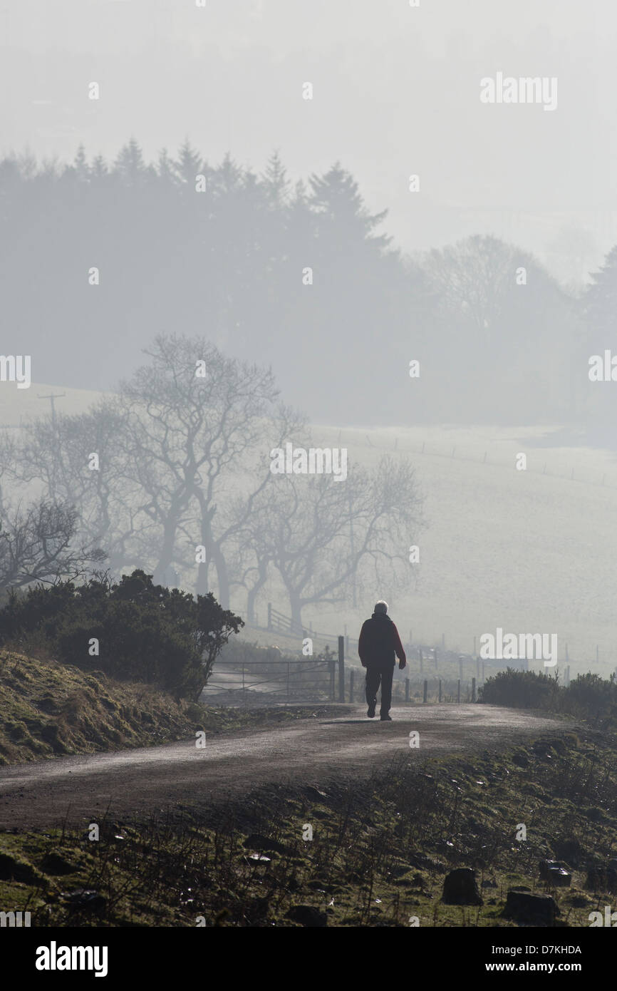 A silhouetted man walks down a country path on a misty and frosty day on the Old Kilpatrick Hills in Scotland Stock Photo