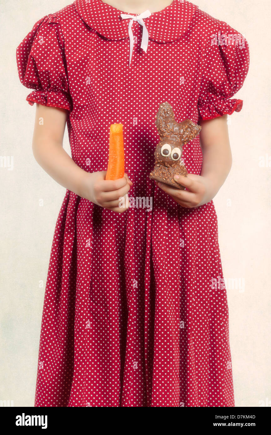 healthy and unhealthy - a girl holding a carrot and a chocolate bunny Stock Photo