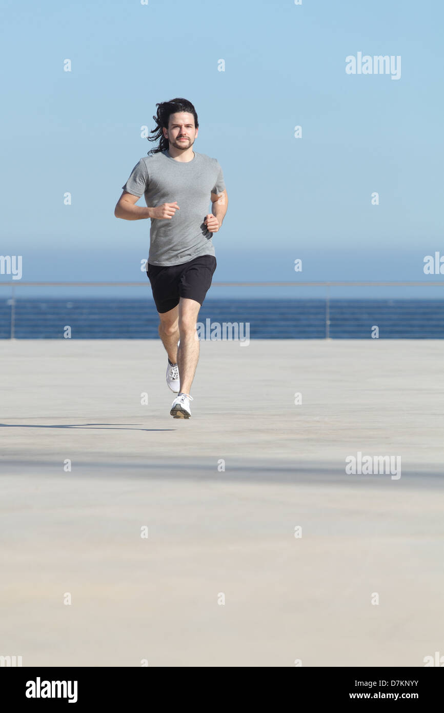 Front view of a sportsman running on the concrete of the seafront with the sea in the background Stock Photo