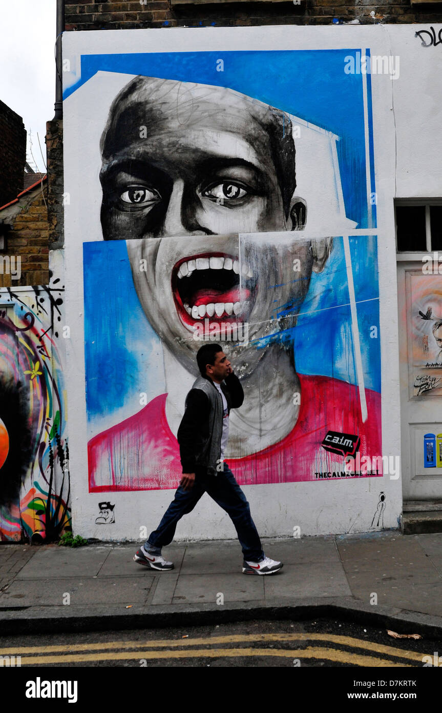 A man walks past a wall covered in graffiti in Brick Lane, London, UK Stock Photo