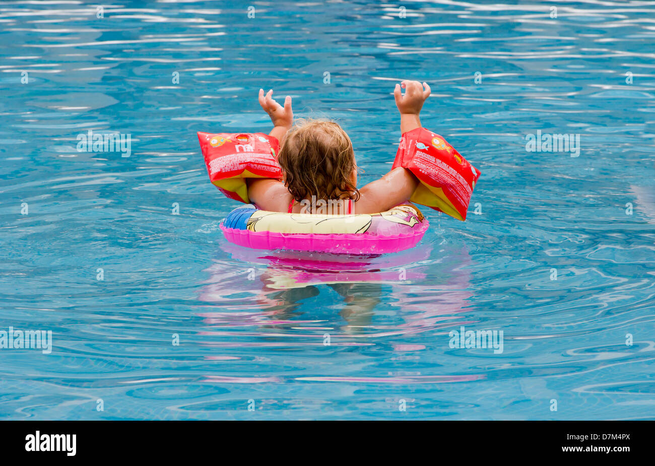 Three year old girl happily playing in swimming pool hires stock