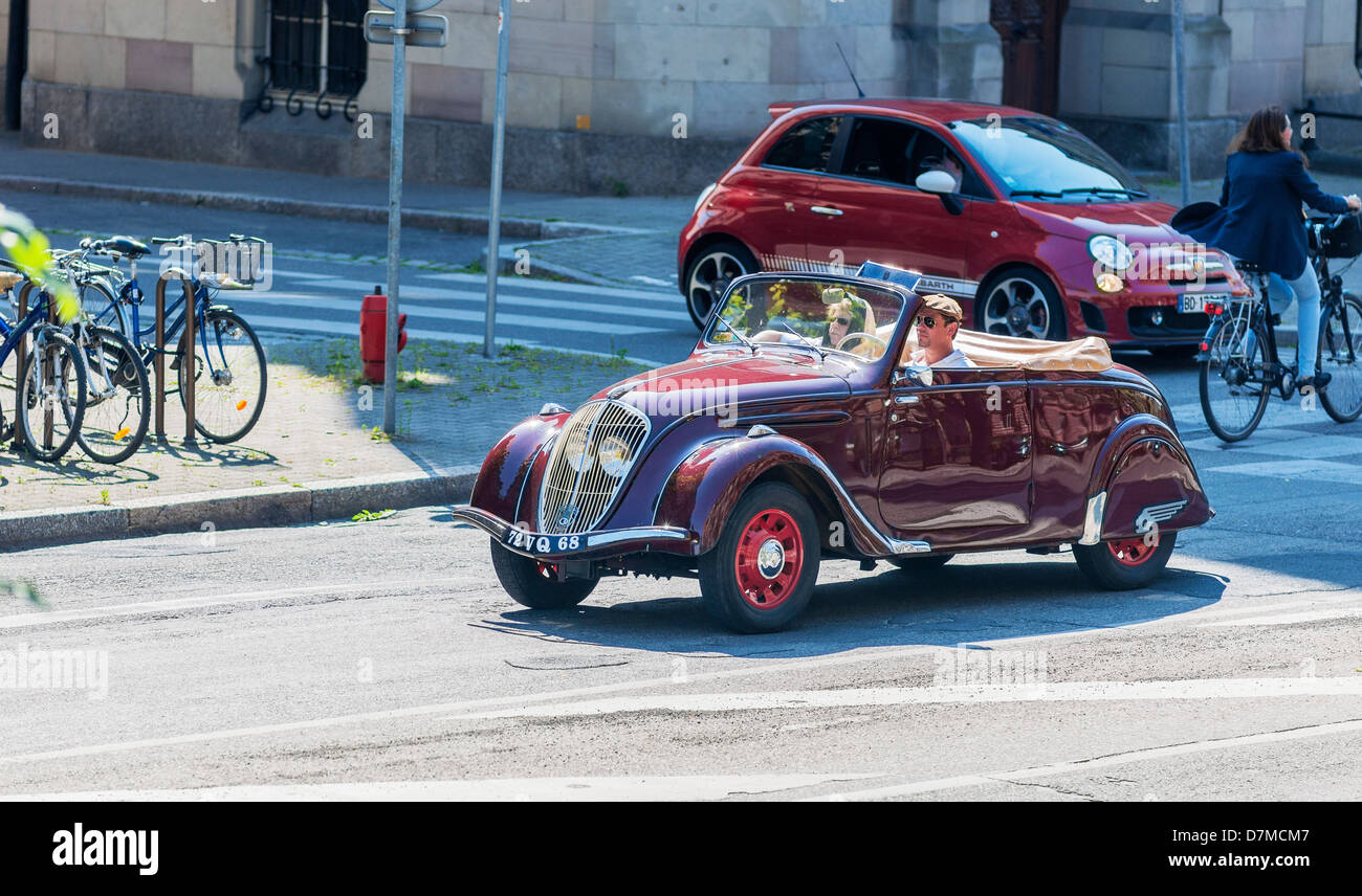 Couple driving a red convertible Peugeot 202 French vintage car, parked red Fiat Abarth car in the distance, Strasbourg, Alsace, France, Europe Stock Photo