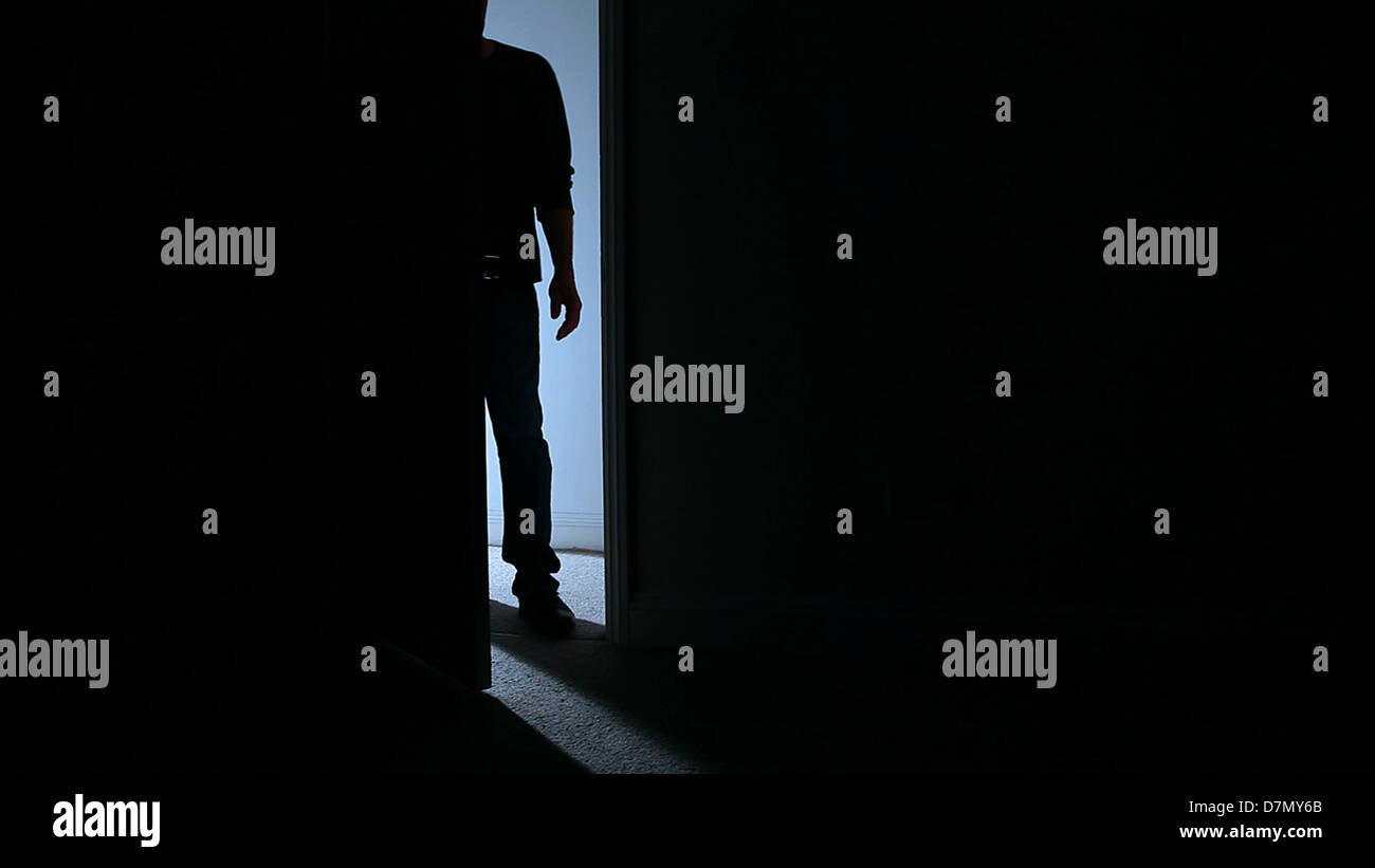 Silhouette of a man standing in an open door leading into a dark room. Stock Photo