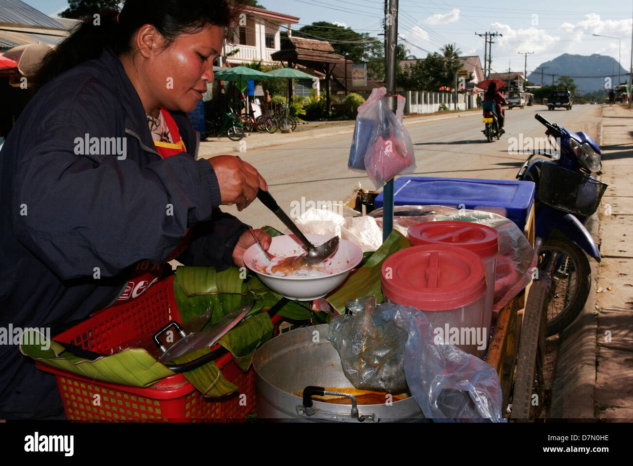 A noddle vendor in Vang Vieng pours spicy soup onto rice noodles, now ready to serve. Stock Photo