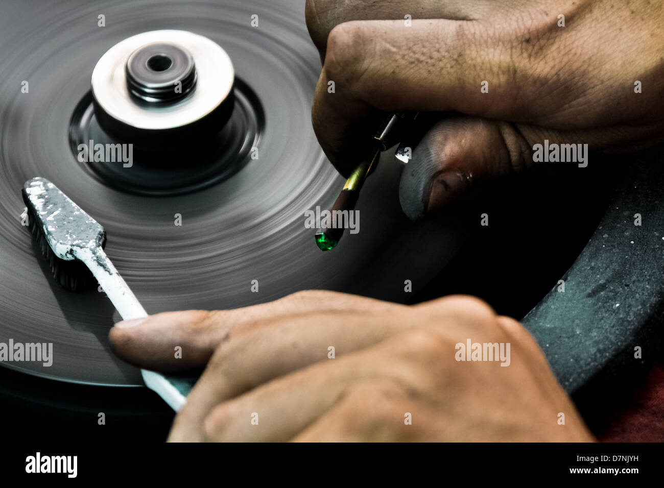 An emerald cutter polishes a gemstone on a faceting machine in a