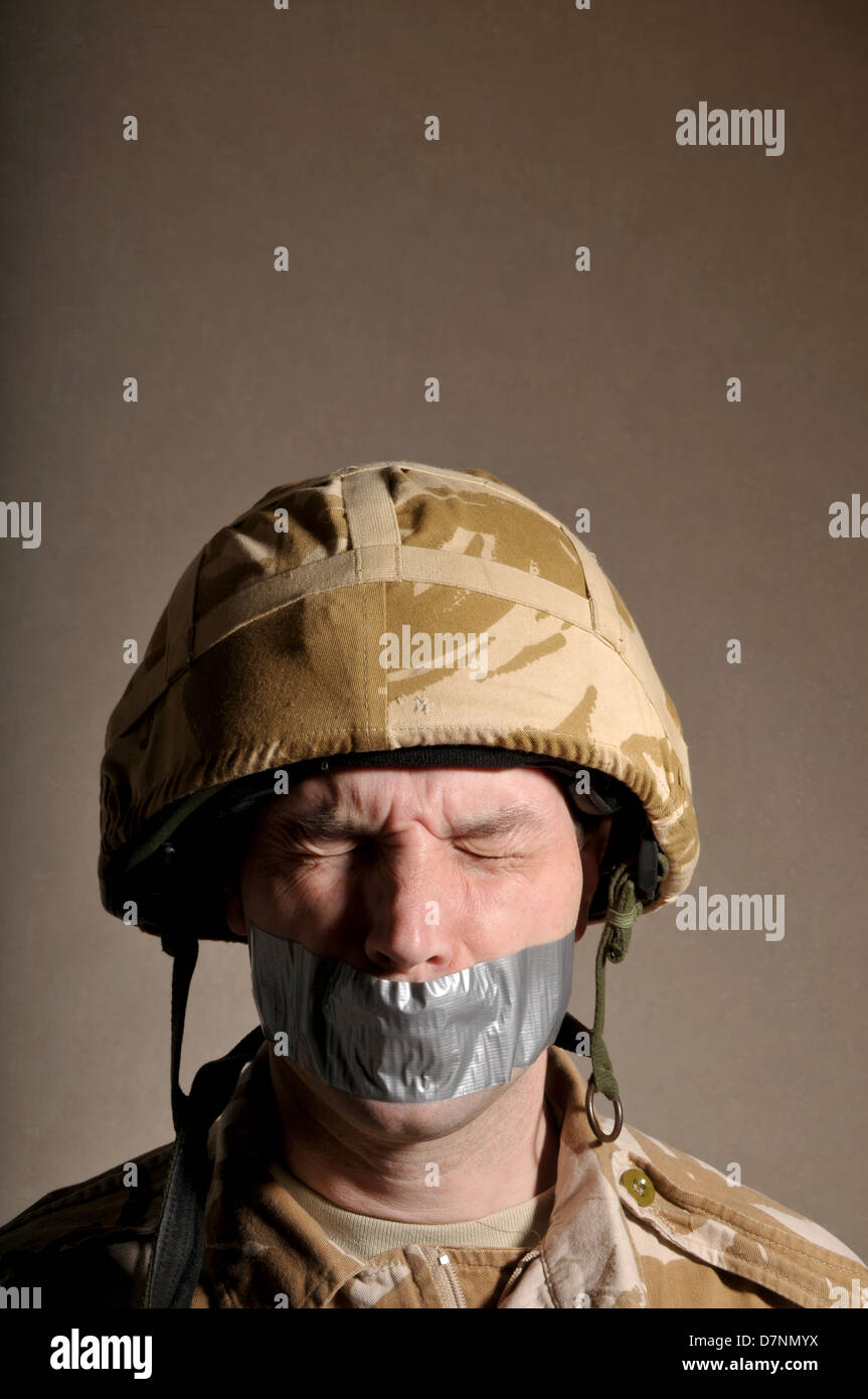 Soldier with his mouth taped over. Soldier is wearing British Military camouflage uniform against a dark background. Stock Photo
