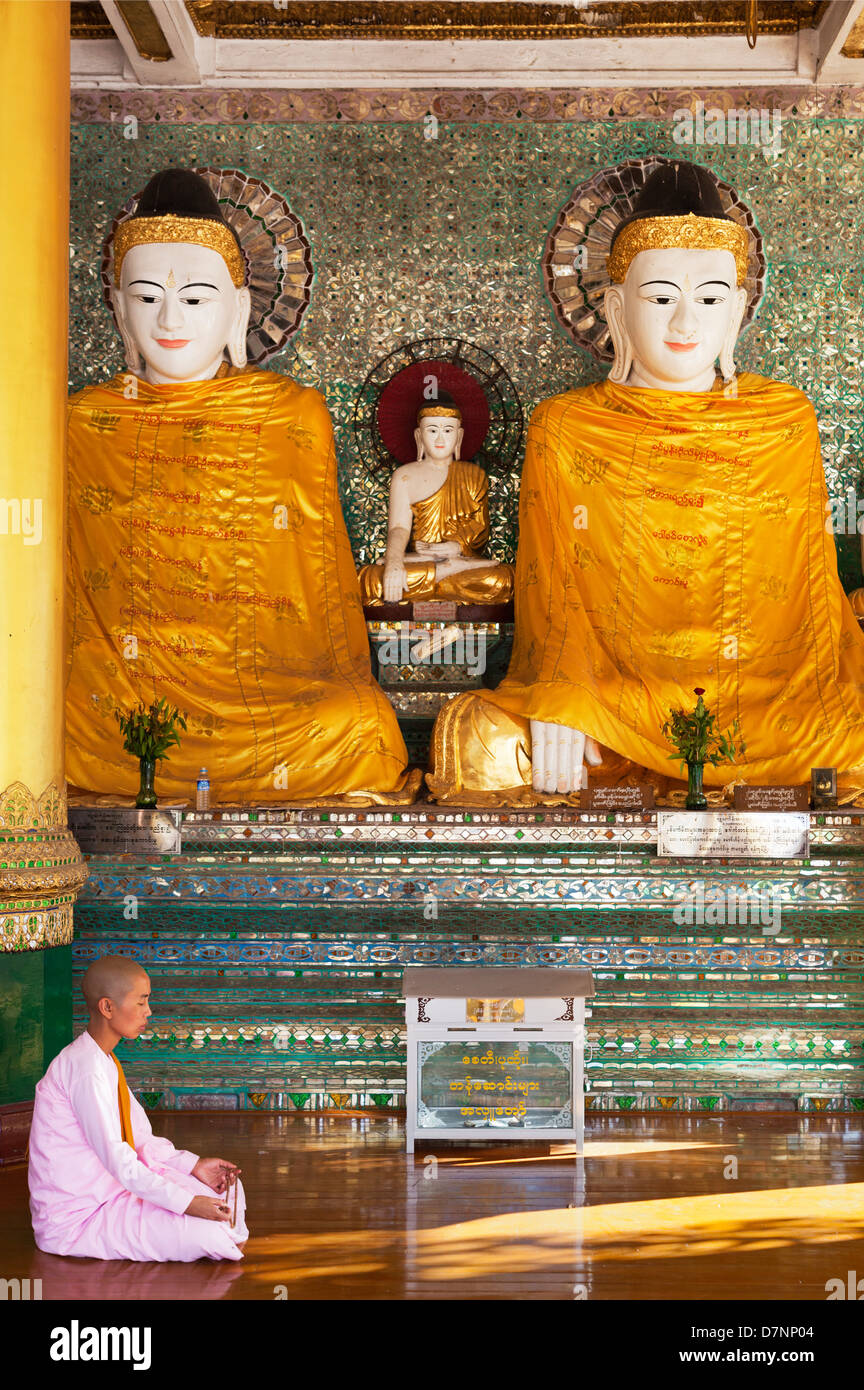 Nun praying before Buddhas in Shwedagon Pagoda, Yangon Myanmar Stock Photo