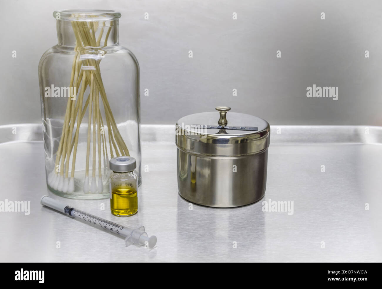 Syringe, medication vial, cotton swabs, and alcohol on a stainless
