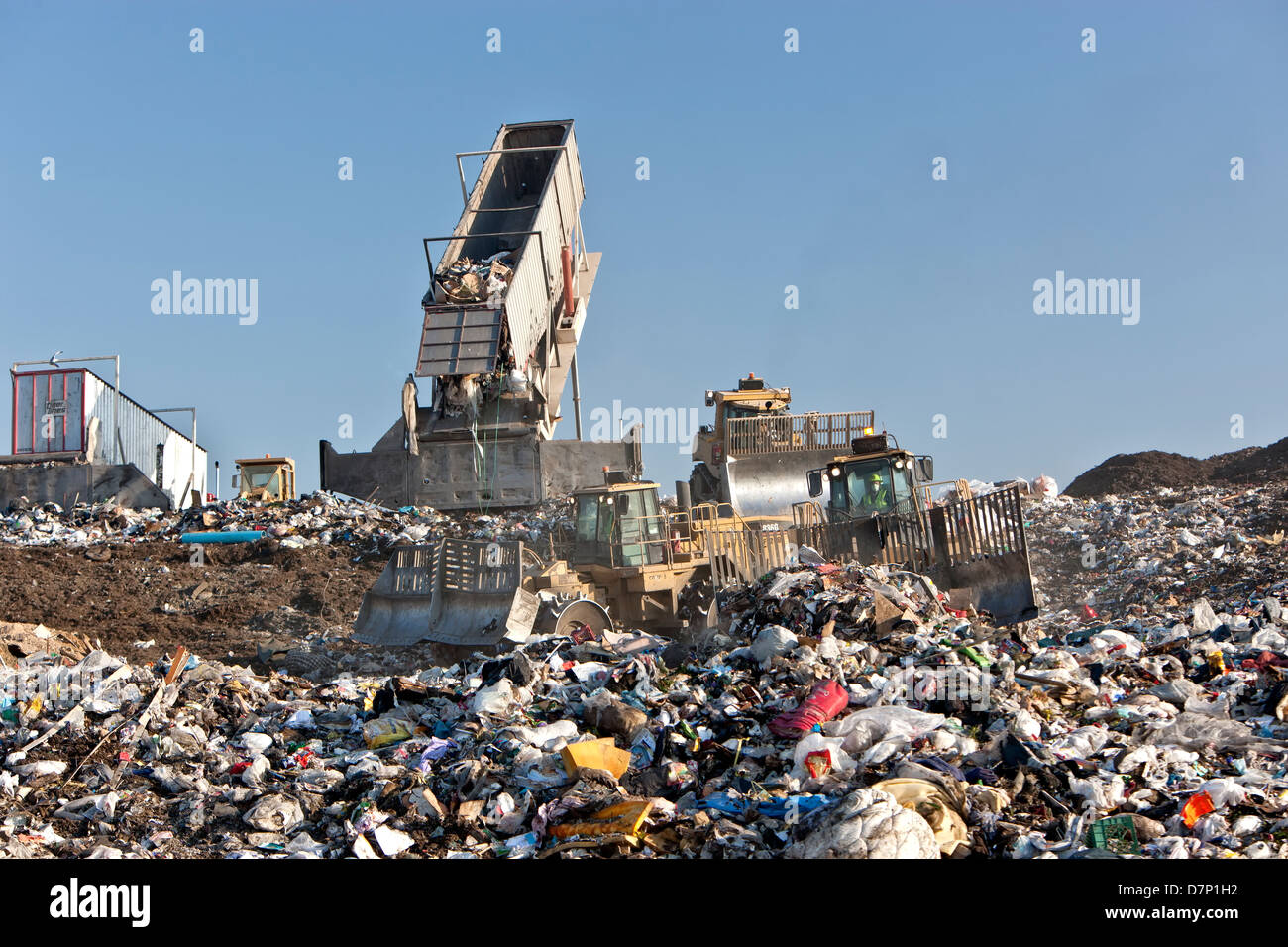Landfill, tractor compactors pushing trash. Tipper dumping semi trailer